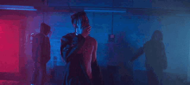 a man without a shirt is standing in front of a group of people in a dark room with hearts in the background .