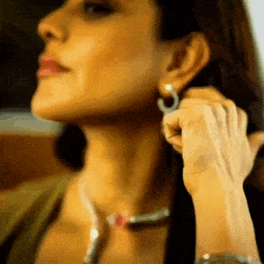 a woman wearing a necklace and hoop earrings adjusts her earrings
