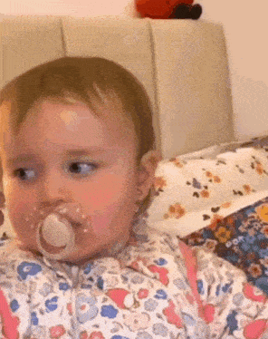 a baby girl with a pacifier in her mouth is sitting on a bed .