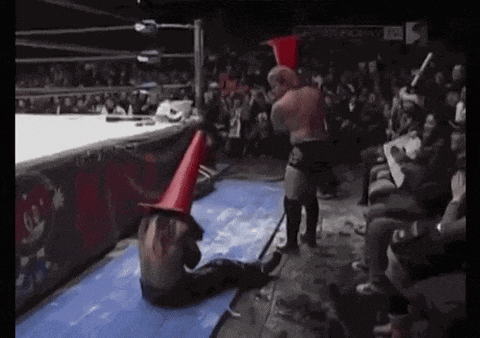 a wrestler wearing a cone on his head is wrestling another wrestler in a ring .