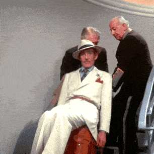 a man in a white suit sits on a suitcase