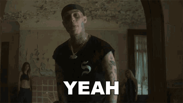 a man with tattoos on his face is saying yeah in a room .