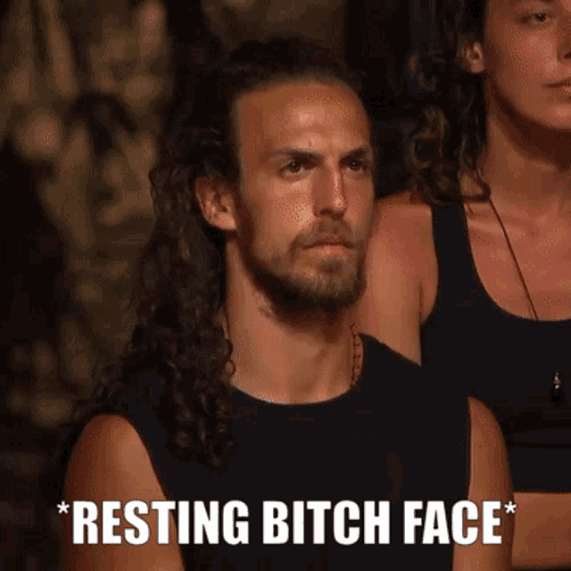 a man with long hair and a beard is sitting next to a woman with the words resting bitch face above him