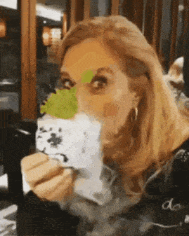 a woman is eating a sandwich with a green leaf on her face