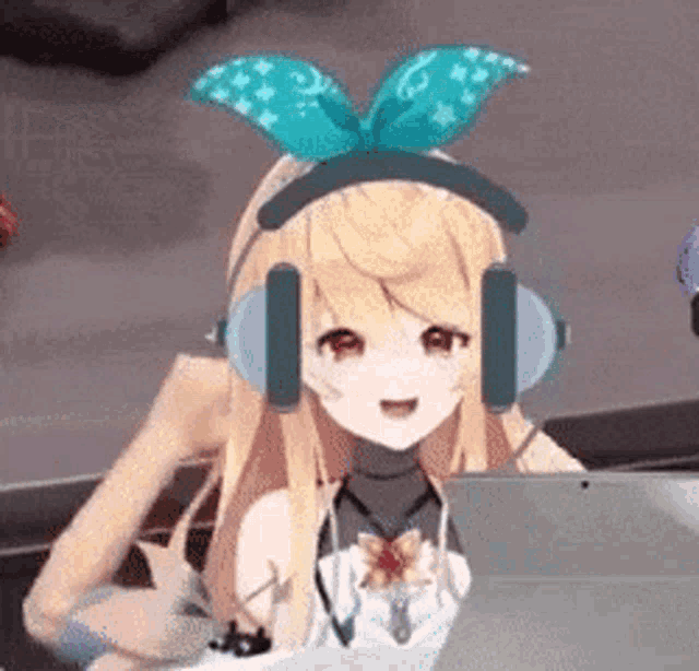 a blonde anime girl wearing headphones and a bow on her head is sitting in front of a laptop computer .