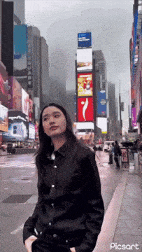 a woman in a black shirt is standing in front of a city street with a sign that says picsart on the bottom