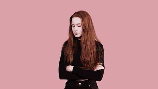 a woman with long red hair is standing with her arms crossed