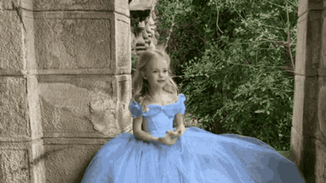 a little girl wearing a blue dress is sitting on a stone wall