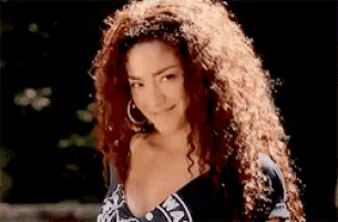 a woman with long curly hair is smiling and wearing a black and white top .