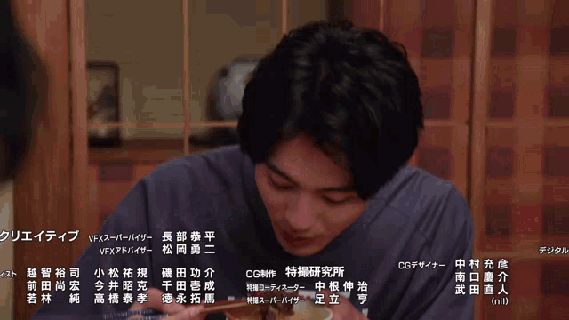a man in a blue shirt is eating a bowl of food with chopsticks
