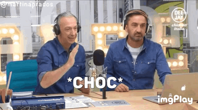 two men wearing headphones are sitting at a table with a laptop and a microphone with choc written on it