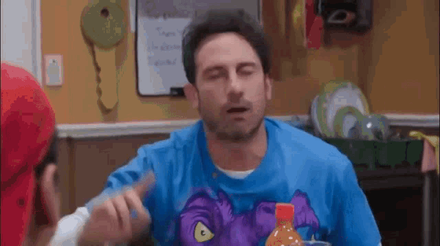 a man in a blue shirt is sitting at a table with his eyes closed and a bottle of orange juice .