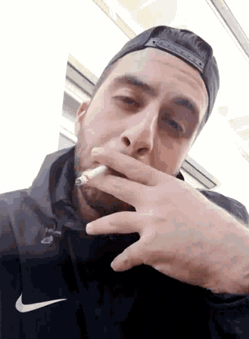 a man smoking a cigarette wearing a black nike jacket