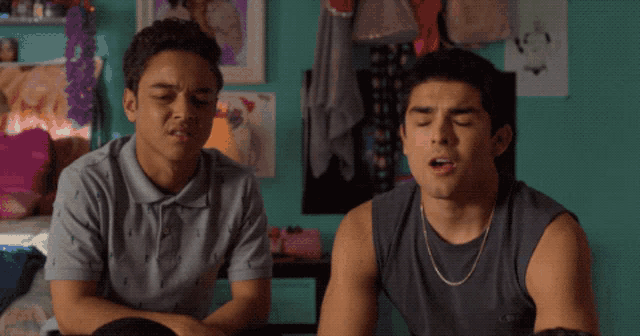 two young men sitting next to each other in a bedroom