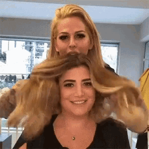 two women are playing with each other 's hair in a hair salon .