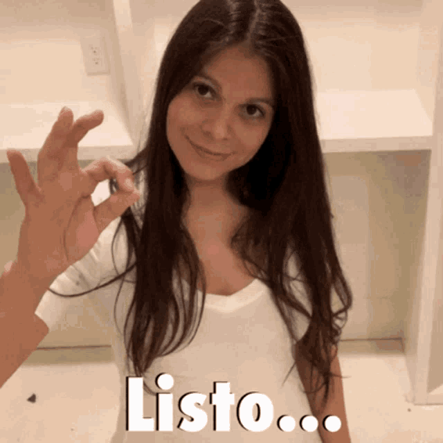 a woman in a white shirt is giving an ok sign with the word listo written below her