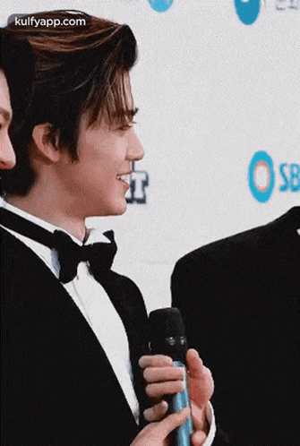 a man in a tuxedo is holding a microphone while smiling .