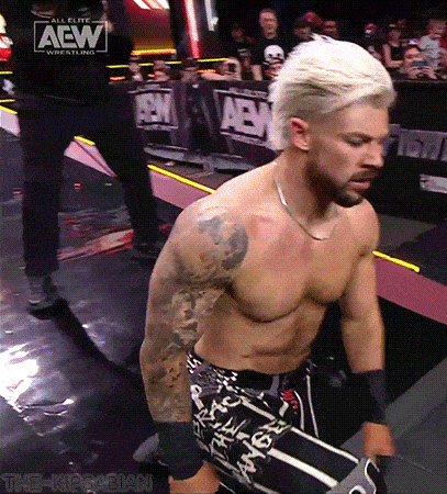 a shirtless wrestler is standing in a ring with a aew logo on the wall behind him .