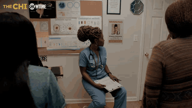a woman in a blue scrub sits in front of a missing poster