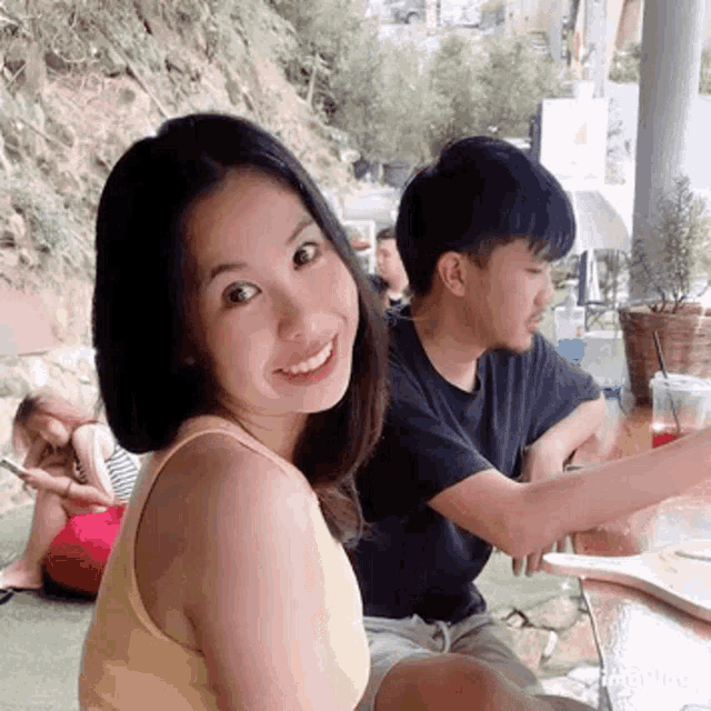 a woman in a yellow tank top smiles while sitting next to a man in a black shirt