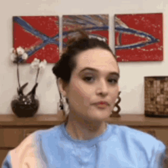 a woman in a blue shirt is making a funny face in front of paintings .