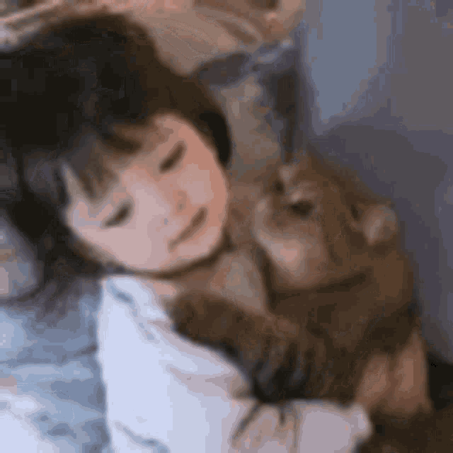 a little girl is laying on a bed holding a small dog .