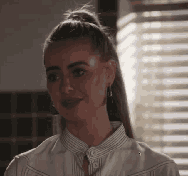 a woman wearing a ponytail and earrings looks at the camera