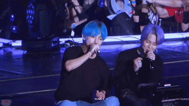 two men are singing into microphones on a stage .