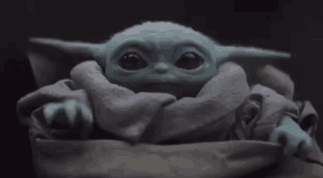 a baby yoda from star wars is sitting in a blanket and waving .