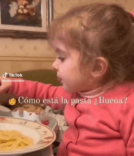 a little girl in a pink shirt is looking at a plate of spaghetti