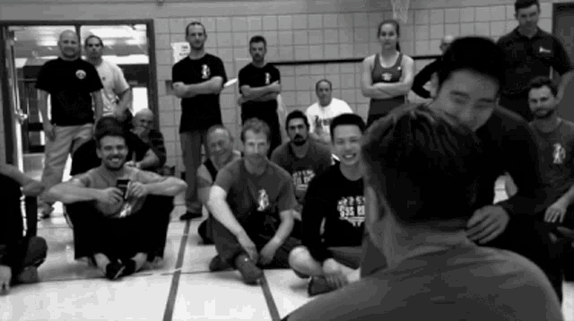 a black and white photo of a group of people with one man wearing a shirt that says ' karate '