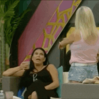 two women are sitting on a couch talking to each other . one woman is wearing a pink tank top and shorts .
