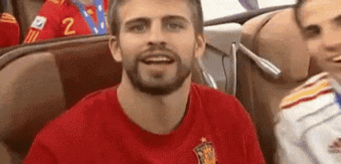 a man with a beard wearing a red shirt is sitting in a chair .