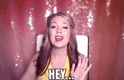 a woman in a yellow shirt is sitting in a chair and saying `` hey '' .