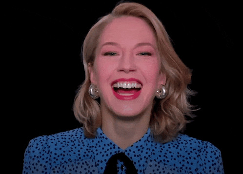 a woman wearing a blue polka dot shirt and earrings is laughing