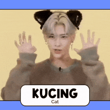 a man wearing cat ears and a sweater with the word kucing on the bottom