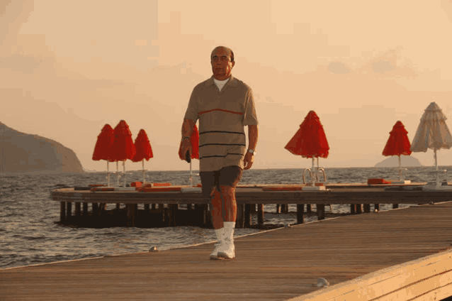 a man walking on a pier with red umbrellas