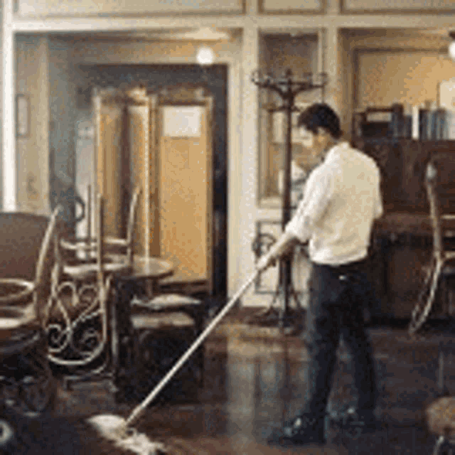 a man is mopping a floor in a room with tables and chairs .