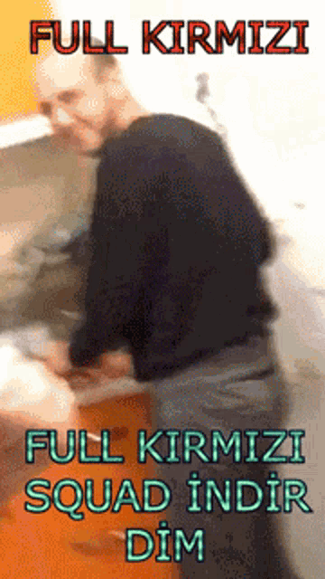 a man in a black shirt is standing in front of a sign that reads full kirmizi full kirmizi squad indir dim