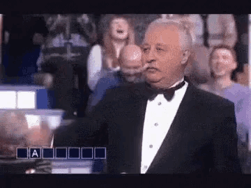 an older man in a tuxedo is standing in front of a crowd .