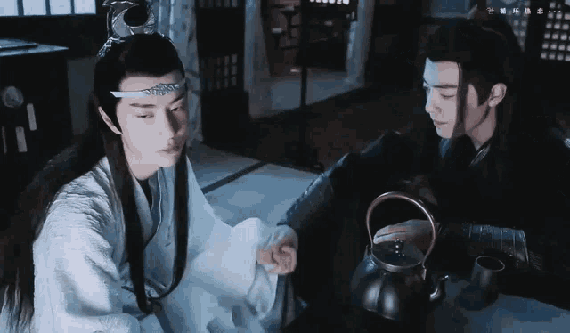 two men are sitting at a table with a teapot and a cup of tea .