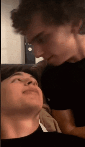 a couple of young men are laying on a couch and kissing each other .