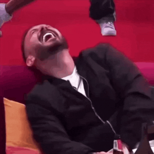 a man in a suit is laughing while sitting on a red couch
