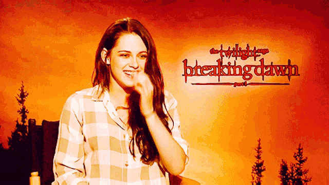a woman laughs in front of a twilight breaking dawn poster