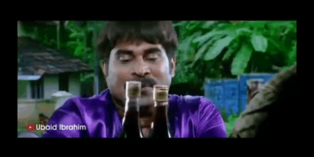 a man in a purple shirt is drinking from a bottle .