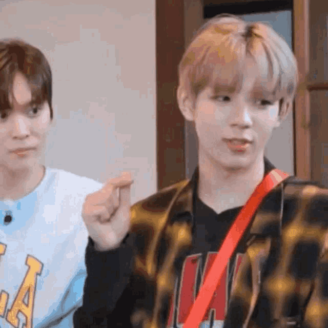 two young men are standing next to each other in a room and one of them is pointing at the camera .