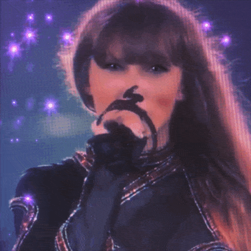 a close up of a woman singing into a microphone with purple lights around her