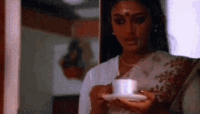 a woman in a white saree is holding a cup of coffee in her hand .