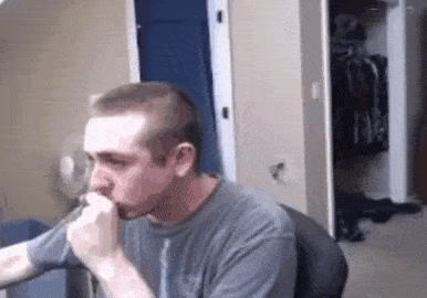 a man is coughing while sitting at a desk in front of a computer .