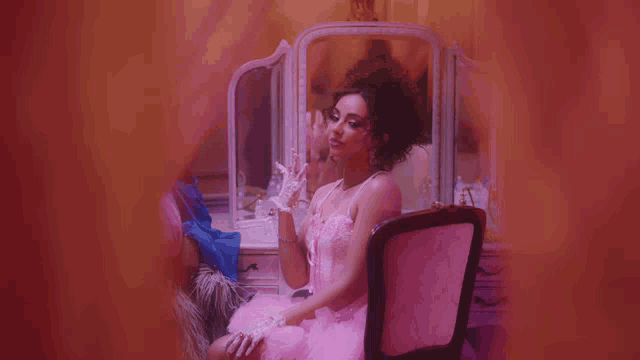 a woman in a pink dress is sitting in front of a pink mirror